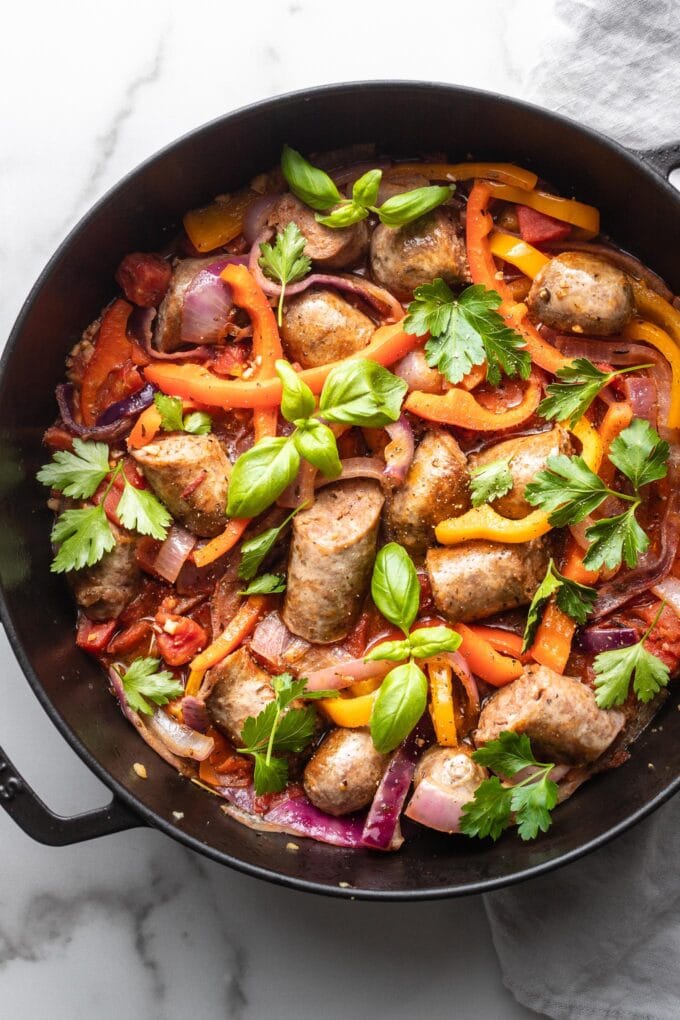 A skillet filled with Italian sausage, peppers, and onions, garnished with herbs and ready to serve.