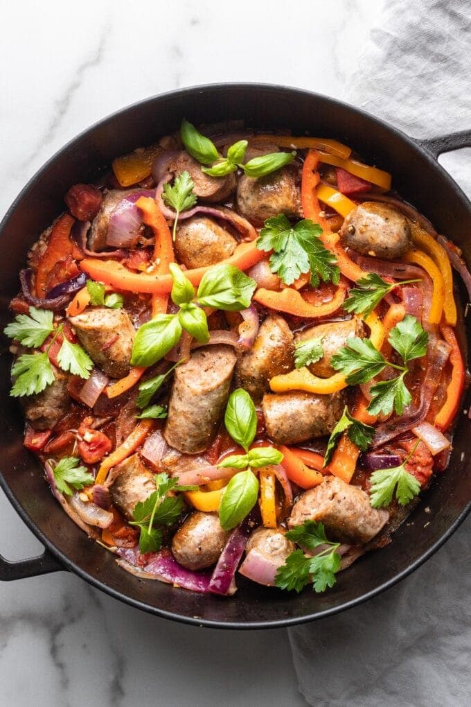 A skillet filled with Italian sausage, peppers, and onions, garnished with herbs and ready to serve.