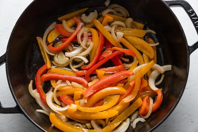 Sliced peppers and onions in a deep cast iron skillet.