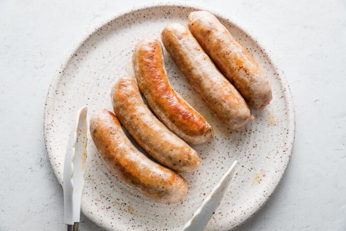 Browned Italian sausages resting on a white ceramic dinner plate.