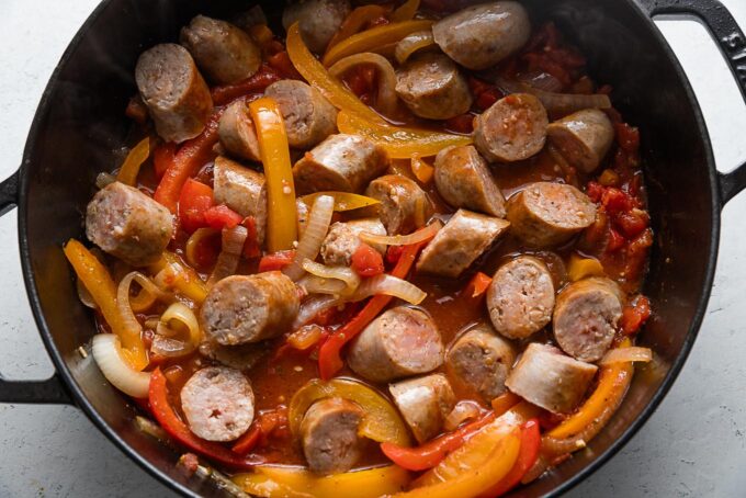 Sliced Italian sausages with peppers and onions in a light tomato sauce simmering in a deep cast iron skillet.