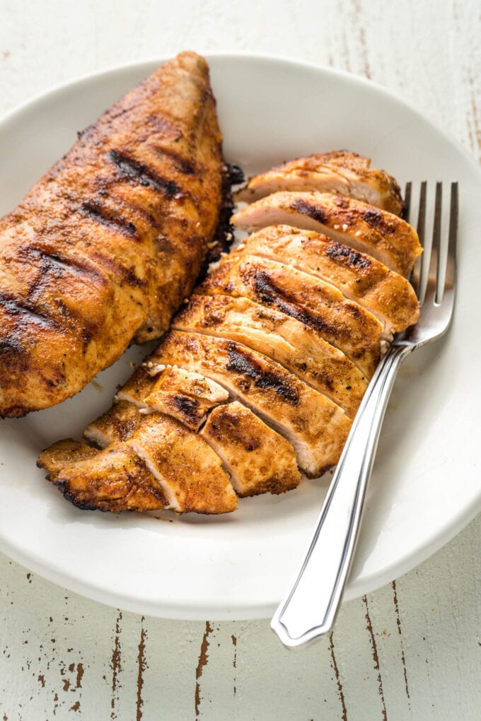 Slices of grilled chicken with dark grill marks on a plate with a fork.