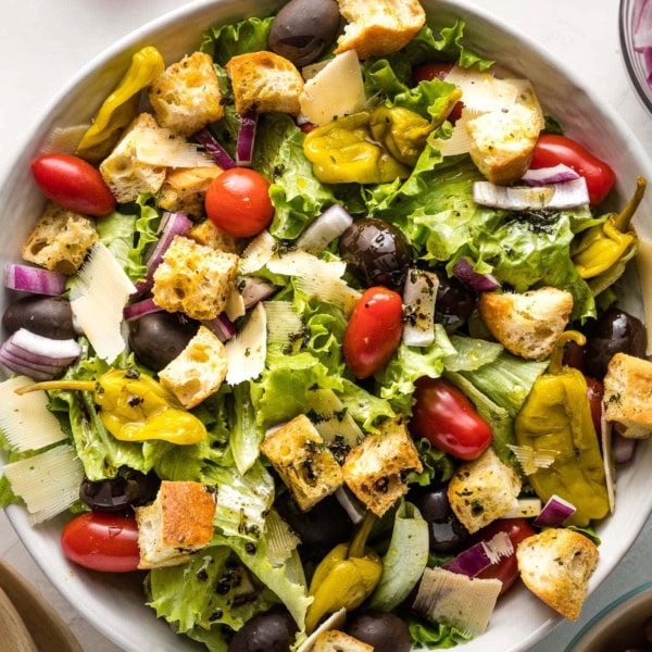 Large bowl of Italian salad with romaine, tomatoes, peppers, olives, and croutons.