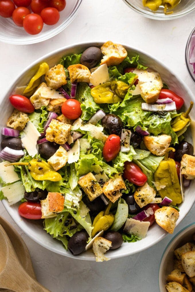 Large bowl of Italian salad with romaine, tomatoes, peppers, olives, and croutons.