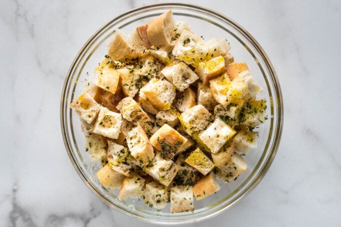 Olive oil, butter, and seasoning drizzled on bread cubes.