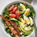 Spinach salad with bacon, hard boiled eggs, avocado, tomatoes, and a vinaigrette dressing.