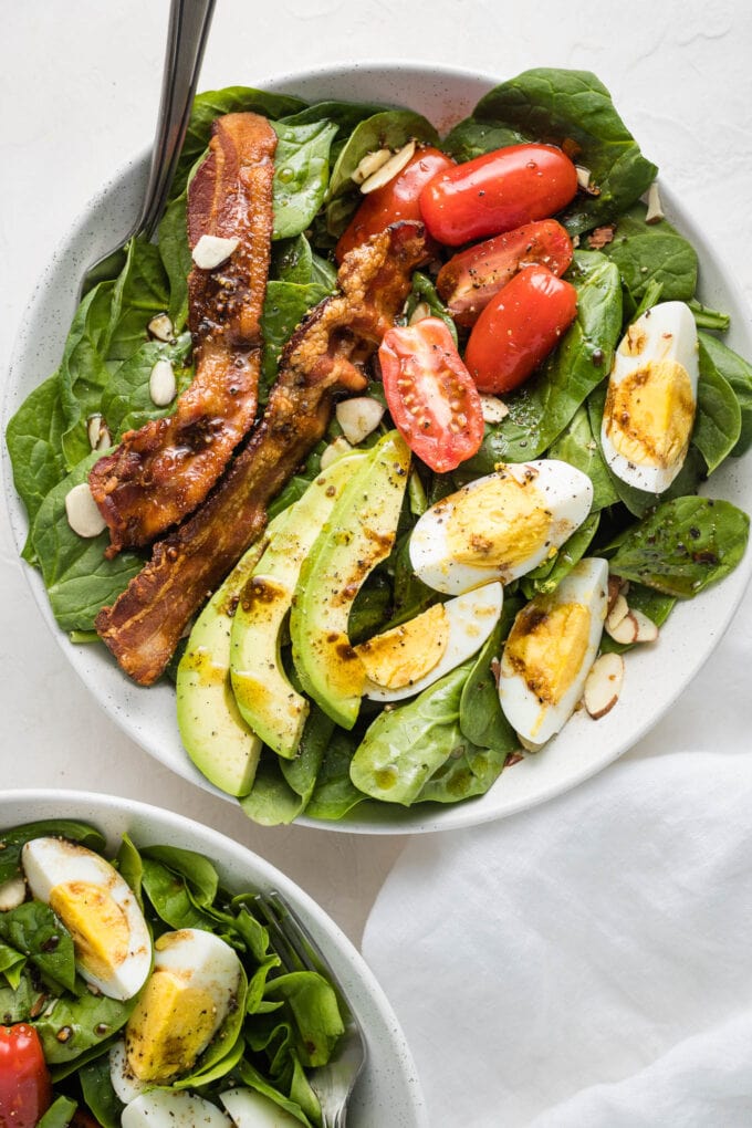 Spinach salad with bacon and eggs in a white bowl.