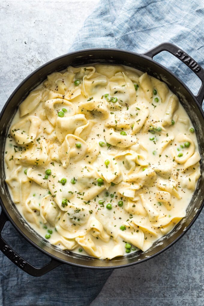 Large cast iron pan full of creamy tortellini Alfredo with peas.