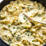 Wooden spoon stirring a creamy Alfredo sauce mixed with tortellini.