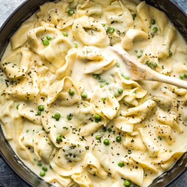 Wooden spoon stirring a pot of creamy tortellini.
