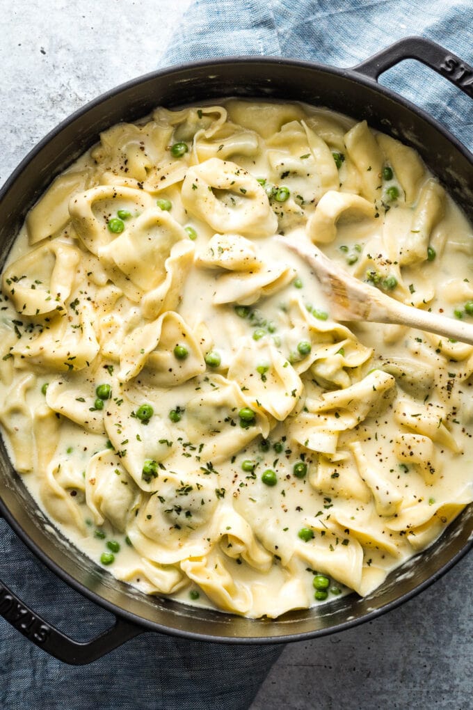 Wooden spoon stirring a pot of creamy tortellini.