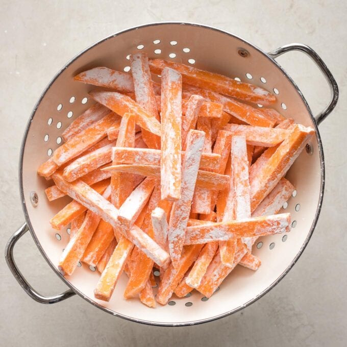 Fries dusted in cornstarch in a colander.