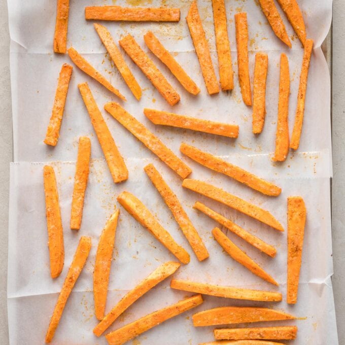 Seasoned, unbaked fries spread out on a parchment-lined pan.
