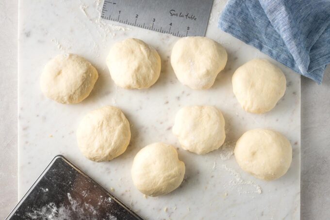 Shaped rolls on the counter with dough scraper and kitchen scale.