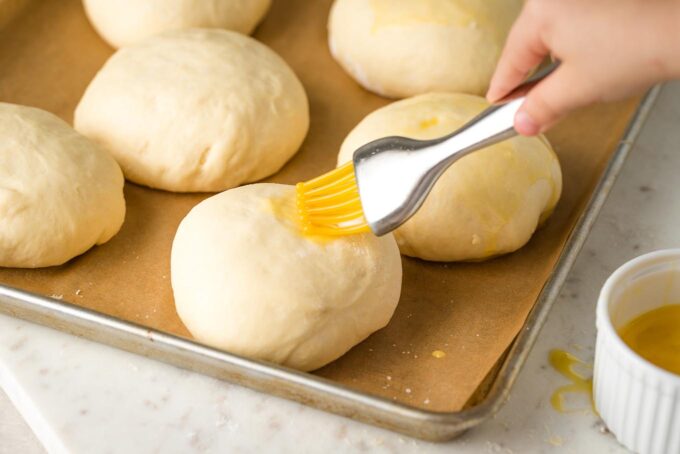 Small hand brushing egg wash on a bun.