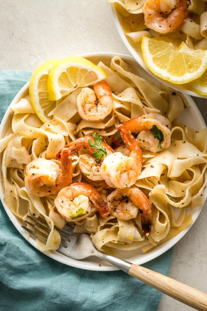 Small white plates with lemon pepper shrimp, pappardelle, and lemon slices for garnish.