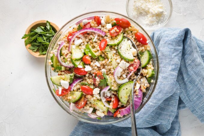 Large bowl of pearl couscous salad with cucumbers, tomatoes, and feta.