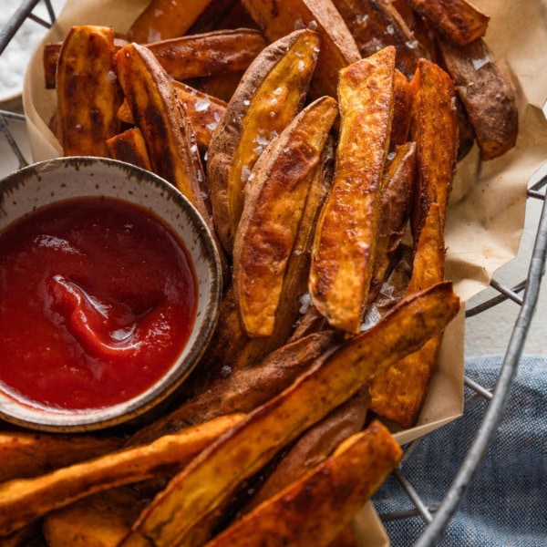 Metal basket full of homemade roasted sweet potato wedges spiced with chili powder and cumin.