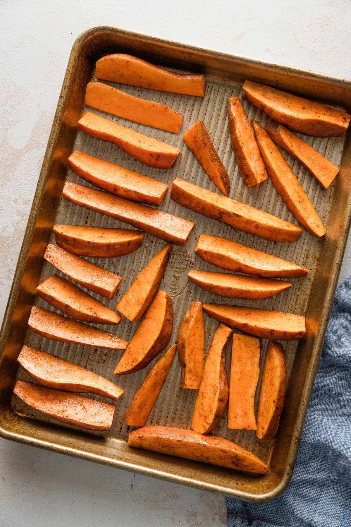 Cut sweet potato wedges arranged with space between them on a rimmed baking sheet.