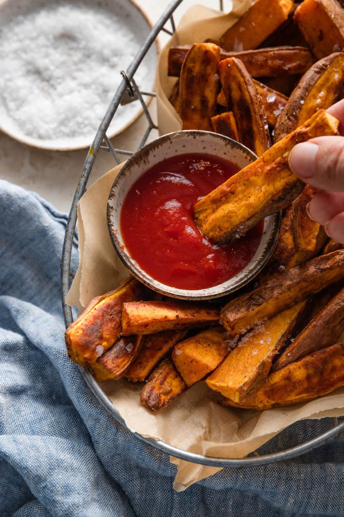 A woman's hand dipping a sweet potato wedge into a small bowl of ketchup.