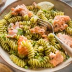 Angled view of a shallow bowl full of pesto pasta with roasted salmon, Parmesan, and lemon.