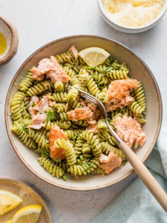 Small pasta bowl filled with salmon pesto pasta with extra grated Parmesan cheese and lemon wedges.