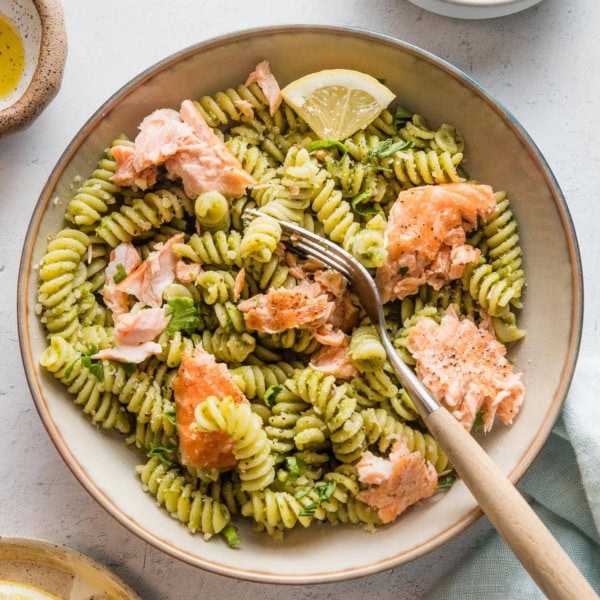 Small pasta bowl filled with salmon pesto pasta with extra grated Parmesan cheese and lemon wedges.