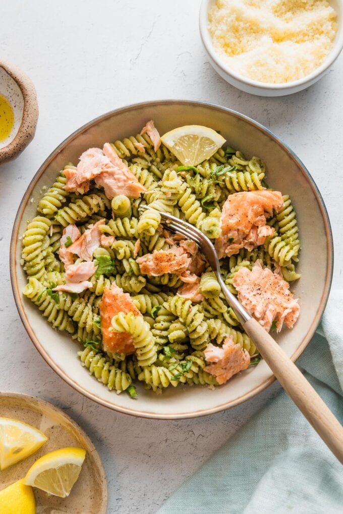 Small pasta bowl filled with salmon pesto pasta with extra grated Parmesan cheese and lemon wedges.