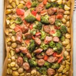 Large sheet pan holding roasted chicken sausage, broccoli, peppers, and baby potatoes.