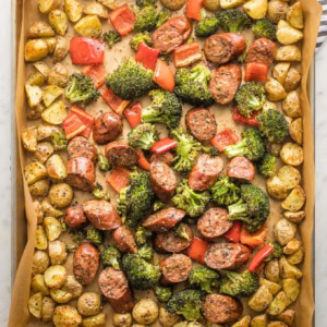 Large sheet pan holding roasted chicken sausage, broccoli, peppers, and baby potatoes.