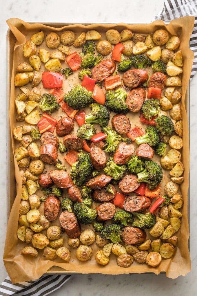 Large sheet pan holding roasted chicken sausage, broccoli, peppers, and baby potatoes.