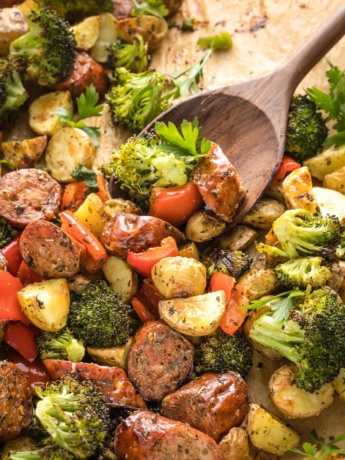 Close-up of spoon scooping up roasted chicken sausage and veggies.