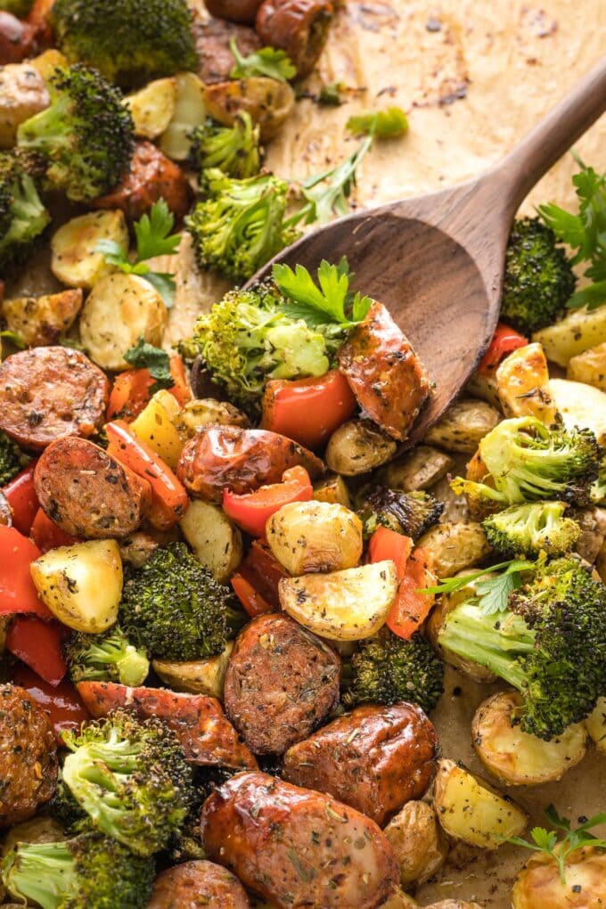 Close-up of spoon scooping up roasted chicken sausage and veggies.