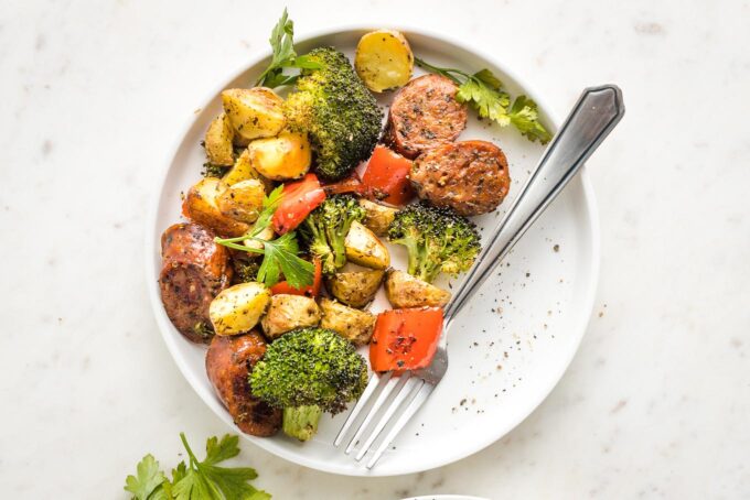 White plate with a serving of chicken sausage, broccoli, pepper, and potatoes.
