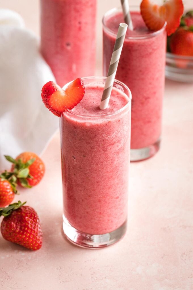 A strawberry pomegranate smoothie in a glass with a straw.