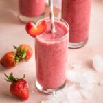 Smoothies in glasses surrounded by ice and strawberries.