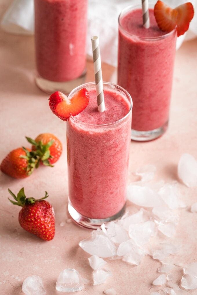 Smoothies in glasses surrounded by ice and strawberries.