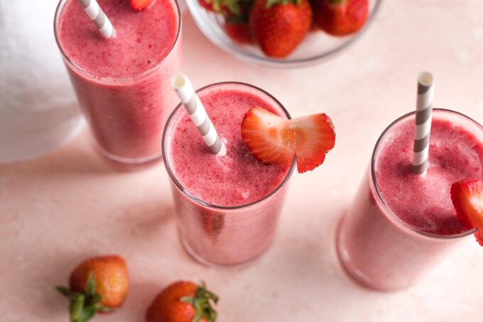 Overhead image of smoothies with straws and strawberry garnish.