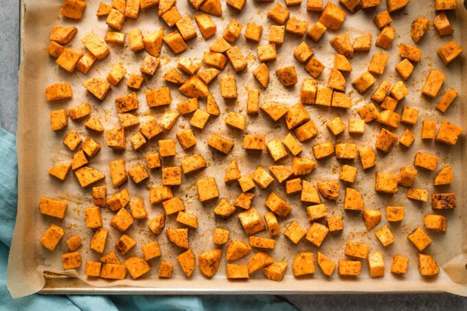 Chopped and seasoned sweet potatoes, uncooked, on a sheet pan.