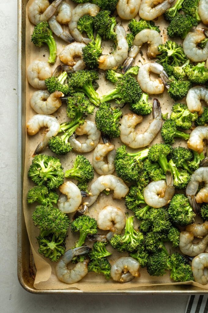 Raw shrimp and half-cooked broccoli on a sheet pan.