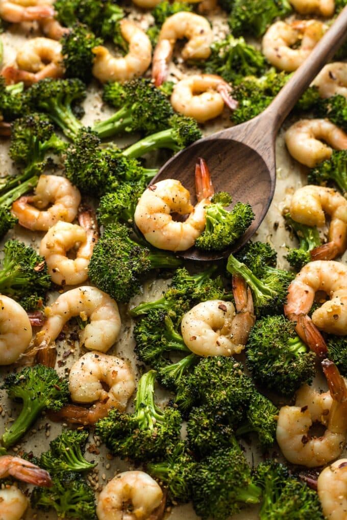 Wooden spoon serving honey garlic shrimp and broccoli off a pan.