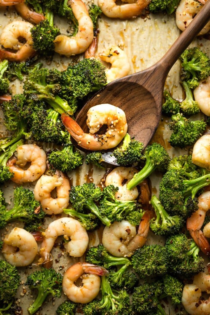 Wooden spoon serving honey garlic shrimp and broccoli off a pan.