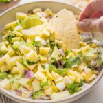 Hand dipping a tortilla chip into fresh mango avocado salsa.