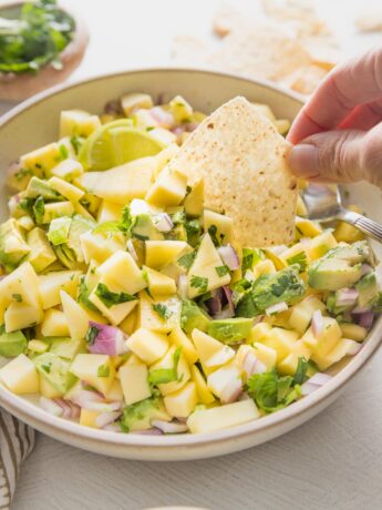 Hand dipping a tortilla chip into fresh mango avocado salsa.