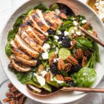 Large salad with spinach, blackberries, cucumber, and grilled chicken, in a white bowl ready to serve.