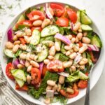 White bowl holding white bean cucumber tomato salad.