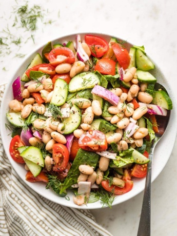 White bowl holding white bean cucumber tomato salad.