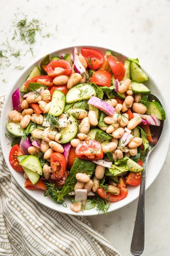 White bowl holding white bean cucumber tomato salad.