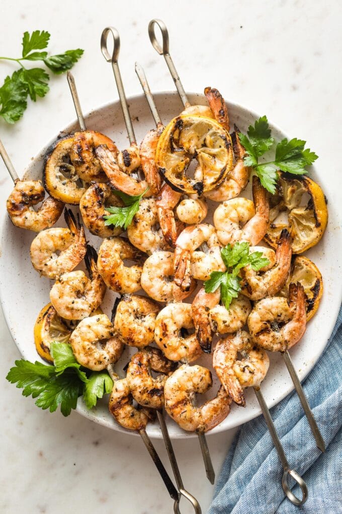 White plate holding Greek-marinated shrimp skewers.