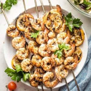 Plate holding grilled Greek shrimp on skewers.